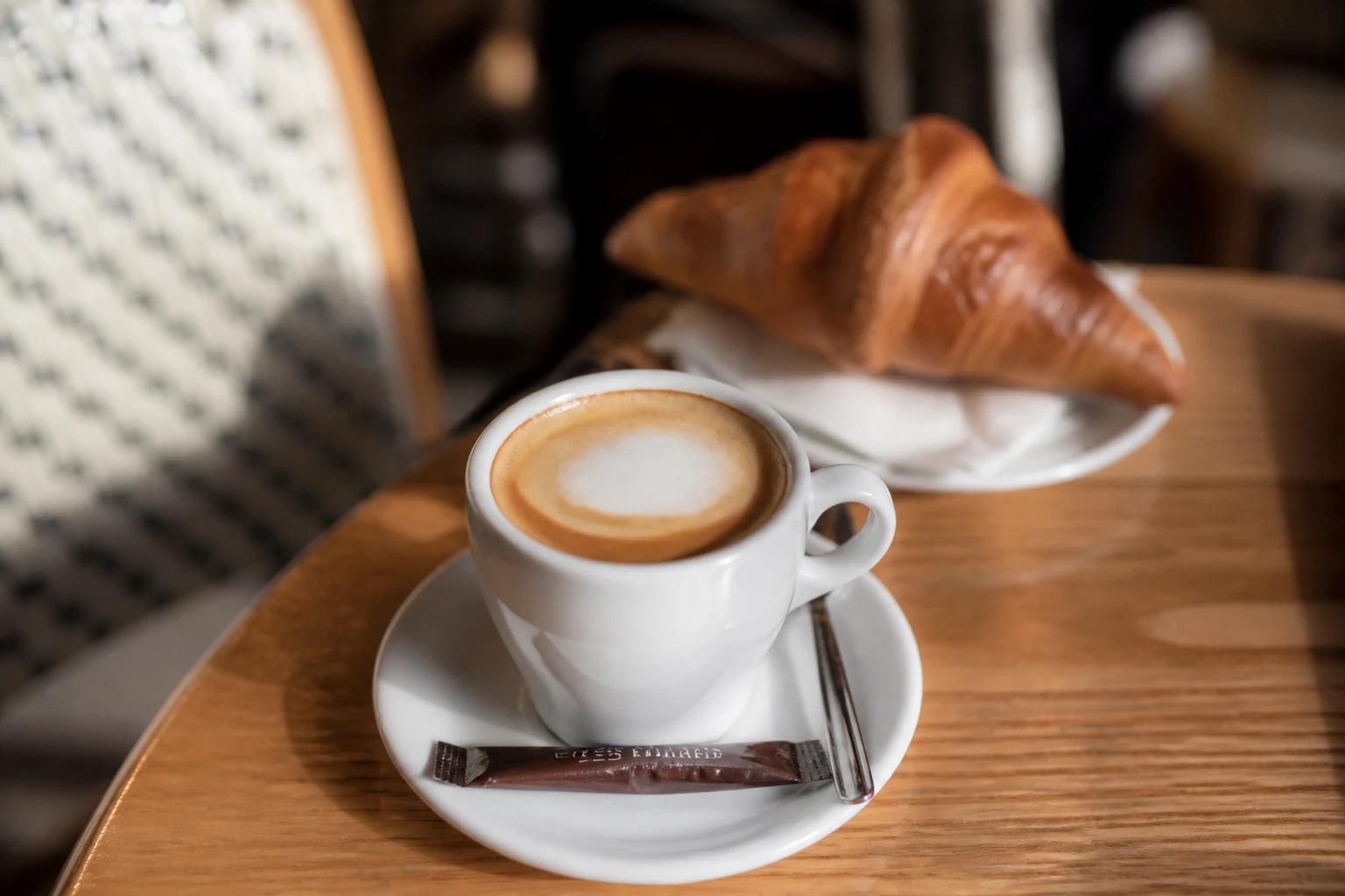 Tasse de café noisette avec mousse légère servie sur une table en bois dans un café parisien
