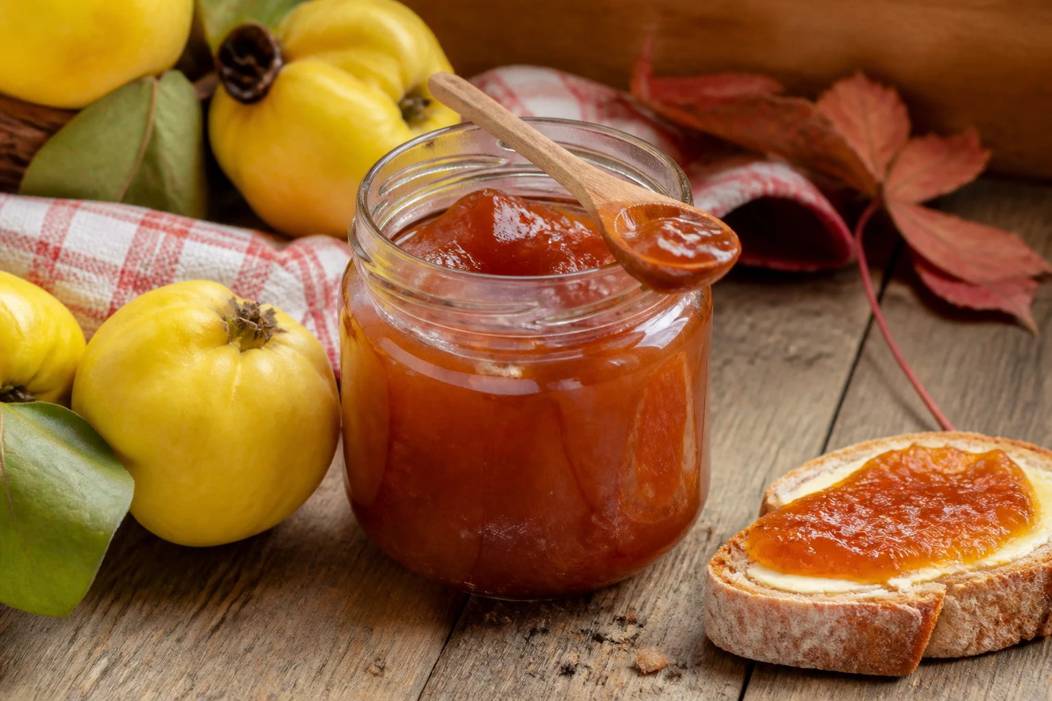 Pot de confiture de coing maison ambrée sur une table en bois avec tartine et coings frais